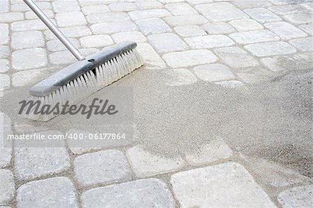 Broom Sweeping Locking Sand Into Backyard Patio Pavers