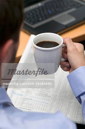 Businessman drinking coffee while reading newspaper in office