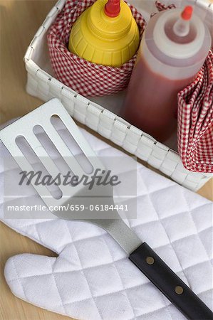 Ketchup and mustard in basket, barbecue glove, spatula