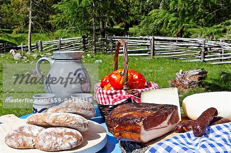 Ein Picknick und Almwiese mit Brot, Speck, Käse, Würstchen, Tomaten und Wein