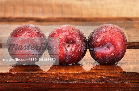 Three plums with droplets of water on wooden crate