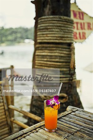 Un verre de jus d'orange fraîchement pressé avec orchidées sur une plage (Thaïlande)