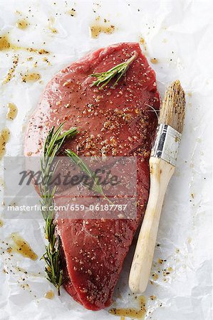 Steak cru dans une Marinade de romarin sur du papier de boucherie ; Pinceau à badigeonner