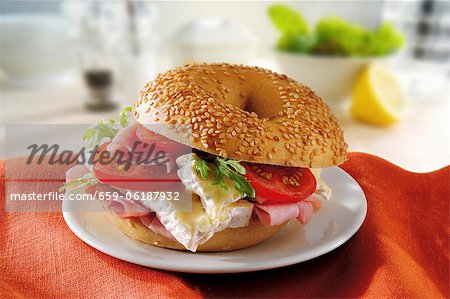 A sesame seed bagel with brie, ham and tomatoes