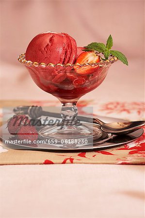 Glasschüssel von Erdbeer-Sorbet mit frischen Erdbeeren und Minze garnieren Glasschüssel von Erdbeer-Sorbet mit frischen Erdbeeren und Minze garnieren