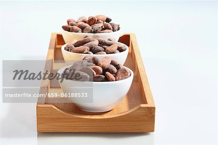 Three bowls of cocoa beans on a wooden board