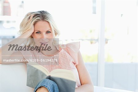 Smiling female lying on a sofa while reading a book