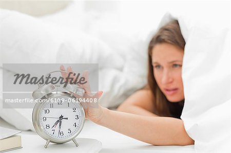 Woman in her bed turning off her alarm clock