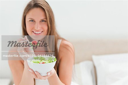 Woman with a bowl of salad offering a tomato to eat
