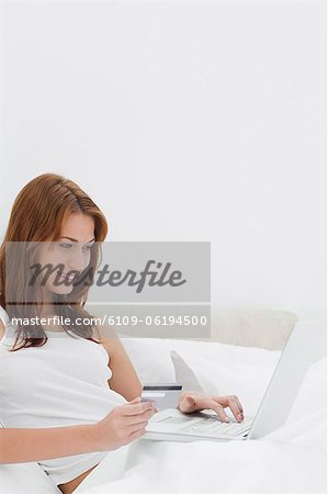 Rothaarige mit ihrer Kreditkarte online sitzen auf ihrem Bett