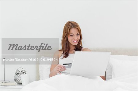 Rothaarige sitzen auf ihrem Bett mit ihrer Kreditkarte online