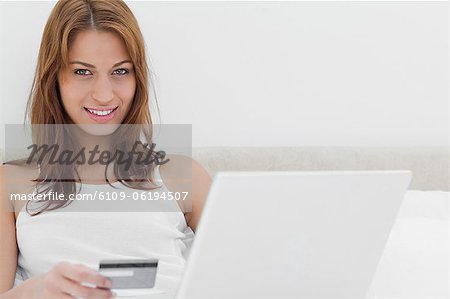 Attractive redheaded sitting on her bed while using her credit card online