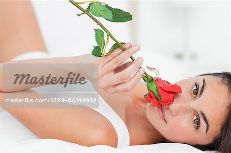 Porträt einer Frau auf dem Rücken liegend, während eine Rose riecht