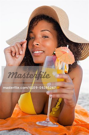 Young attractive woman holding her hat brim while lying down with a cocktail