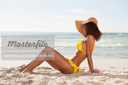 Side view of a young woman sitting on the beach in beachwear