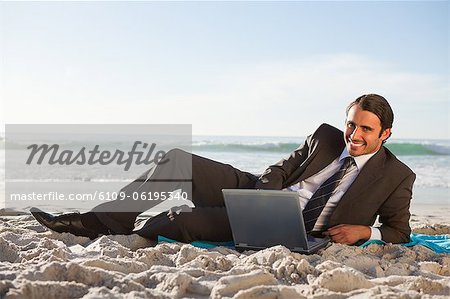 Homme d'affaires souriant à l'aide d'un ordinateur portable sur la plage