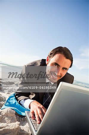 Homme d'affaires souriant à l'aide d'un ordinateur portable tout en se trouvant sur la plage