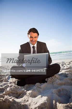 Smiling businessman sitting cross-legged in front of the ocean