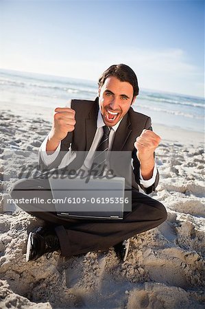 Successful businessman raising his two fists while sitting on the beach
