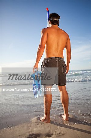 Young attractive man standing on the beach with a snorkel and fins