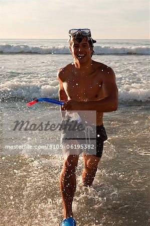 Young happy man wearing a snorkeling equipment while running in the water