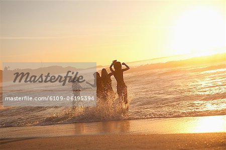 Junge glückliche Frauen tanzen im Wasser bei Sonnenuntergang