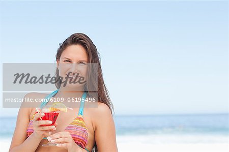 Woman smiling as she holds a cocktail while standing by the sea
