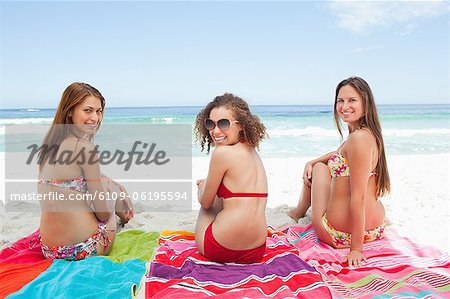 Three friends smiling as they look over their shoulders while sitting on blankets