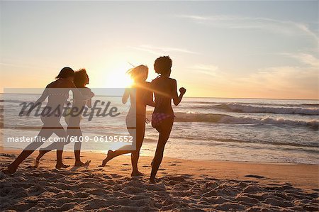 Four friends running across sand