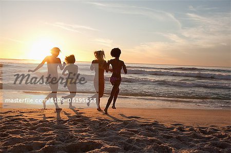 Four friends running across sand with the horizon in the background