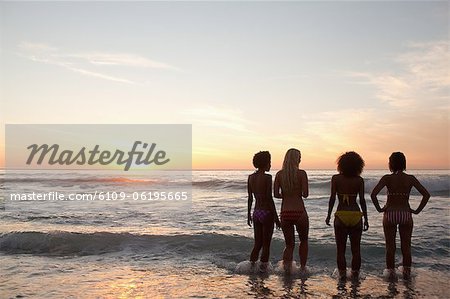 Quatre amis, regarder le coucher du soleil tout en se tenant près des vagues