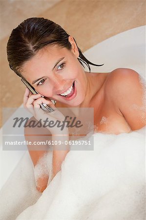 Surprised looking woman with her cellphone in the tub