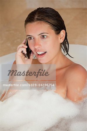 Erstaunt schauende Frau mit ihrem Handy in der Wanne Erstaunt schauende Frau mit ihrem Handy in der Wanne