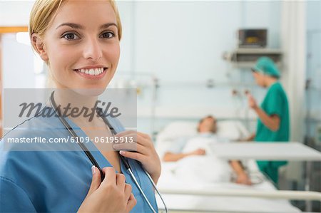 Blonde nurse smiling while touching a stethoscope