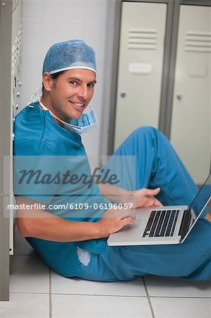 Chirurgien assis sur le sol de la petite armoire tout en utilisant un ordinateur portable