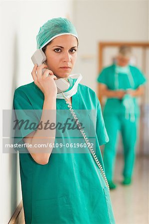 Serious woman surgeon holding a telephone in a hallway