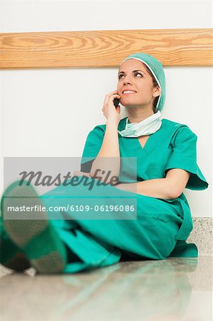 Surgeon sitting on the floor and phoning with her legs crossed
