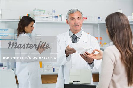 Smiling pharmacist standing giving medicine to a client