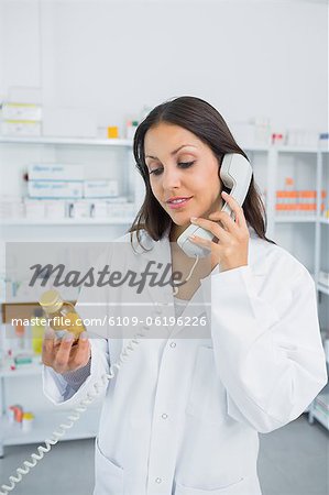 Female pharmacist holding pills while phoning