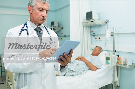 Médecin sérieux en utilisant une tablette tactile en se tenant debout dans une salle d'hôpital lit