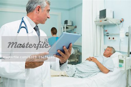 Doctor using a tactile tablet while looking at a patient in a bed ward