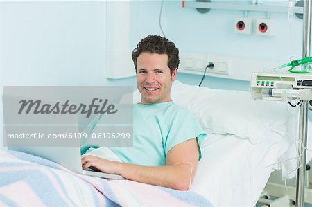 Joyful patient with a laptop lying on a bed