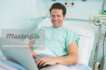 Patient en tapant sur un ordinateur portable tout en couché sur un lit et rire