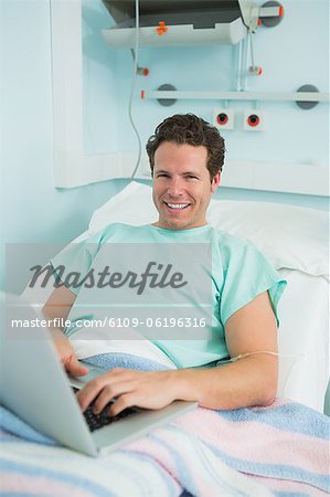 Patient using a laptop while lying on a bed and laughing