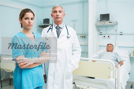 Arzt und Krankenschwester mit ihren Armen gefalteten stehen im Zimmer eines Patienten