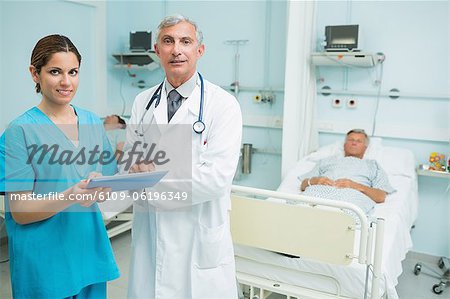 Male doctor and female nurse standing in a room while holding a tactile tablet