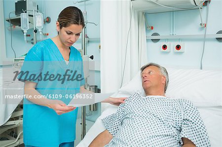 Nurse talking to a patient lying on a bed while holding a paper