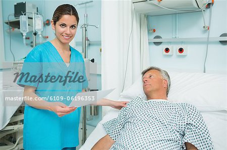 Souriant infirmière toucher l'épaule d'un patient couché sur un lit tout en tenant un livre