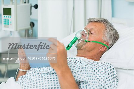 Senior homme patient allongé sur un lit avec un masque tout en maintenant une tablette tactile
