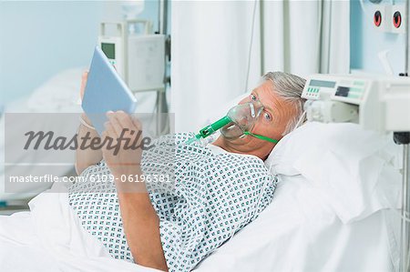 Senior patient holding a tactile tablet in his hands while wearing an oxygen mask